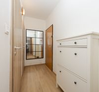 Ein enger Flur mit einem Boden in Holzoptik, einem Spiegel und einem weißen Schuhschrank.