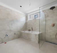 Ein Badezimmer in einem Einfamilienhaus mit Badewanne und Dusche, gefliest mit hellen Fliesen.