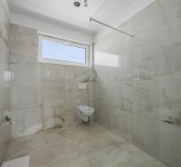 Badezimmer eines Einfamilienhauses mit Wänden und Boden in Fliesen in hellen Farbtönen.