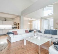 Heller Wohnbereich mit Kamin, Sofas, Küche und Holzboden in einer Ferienwohnung.
