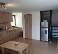 Innenraum einer Hütte mit Küchenzeile, Kühlschrank und Treppe, Boden mit Holzdekor.