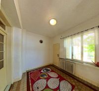 In einem Einfamilienhaus gibt es ein Zimmer mit einem bunten Teppich, einem Fenster und einer Wand mit einem Heizkörper.