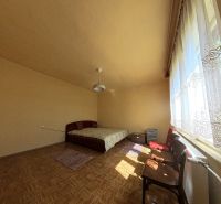 Helles Zimmer im Einfamilienhaus mit Bett, großem Fenster und Boden in Holzoptik.