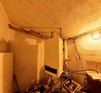 Badezimmer in einem Einfamilienhaus mit Einrichtung und Rohrleitungen, beleuchtet von einer Glühbirne.
