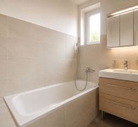 Badezimmer in einem Einfamilienhaus mit Badewanne, Waschbecken und Schrank in Holzdekor.
