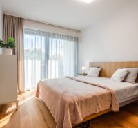 Schlafzimmer in einer 2-Zimmer-Wohnung mit Bett, Vorhängen, Nachttischen und einem Boden mit Holzdekor.