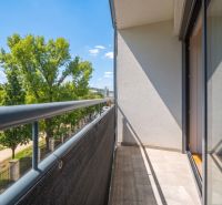 Balkon einer 2-Zimmer-Wohnung mit Blick auf Grünflächen und blauen Himmel.