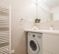 Badezimmer mit hellen Fliesen, Waschmaschine, Waschbecken und Handtüchern in einer 2-Zimmer-Wohnung.
