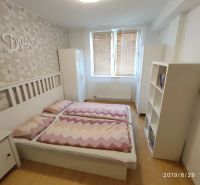 Schlafzimmer mit Bett, Holzboden und Blumenklebeband in einer Zweizimmerwohnung.