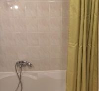 Badezimmer mit weißen Fliesen und einer Badewanne mit Vorhang in einer Zweizimmerwohnung.