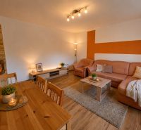Wohnzimmer in einer 3-Zimmer-Wohnung mit Kamin, orangefarbener Wand und Boden in Holzoptik.