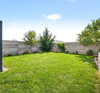 Garten eines Einfamilienhauses in Hrubá Borša mit Rasen, Bäumen und Terrasse.