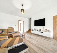 Wohnzimmer in einem Einfamilienhaus mit beigem Sofa und Boden in Holzoptik.
