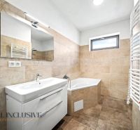 Badezimmer in einem Einfamilienhaus mit Waschbecken, Eckbadewanne und Fliesen in Beigetönen.