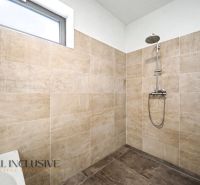 Eine Duschkabine im Einfamilienhaus mit hellen Fliesen und einer modernen Dusche.