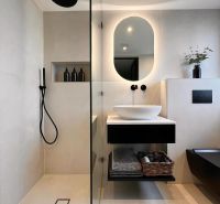 Ein Badezimmer in einem Einfamilienhaus mit beleuchtetem Spiegel, schwarzen Accessoires und einer Dusche.