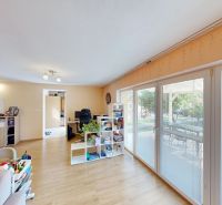 Wohnzimmer in einem Einfamilienhaus mit großen Fenstern und einem Boden in Holzoptik.