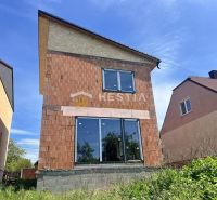 Ein Einfamilienhaus in Cerová mit unvollendeter Ziegelfassade und großen verglasten Türen.