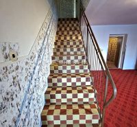 Eine Treppe in einem Einfamilienhaus mit kariertem Fliesenmuster und einem markanten Geländer.
