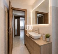 Badezimmer in einer 3-Zimmer-Wohnung mit Waschbecken und beleuchtetem Spiegel an der Wand.