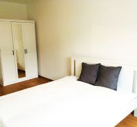 Schlafzimmer in einer 2-Zimmer-Wohnung mit einem weißen Bett und einem Kleiderschrank auf Holzboden.