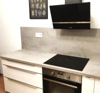 Küche in einer 2-Zimmer-Wohnung mit Kochfeld, Backofen und einem Bild mit Kräutern.