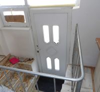 Treppen und Eingangstür in einer 2-Zimmer-Wohnung mit Geländer und Mosaikfliesen.