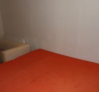 Ein Zimmer mit einem orangefarbenen Bett und einem beigen Sessel in einer Zweizimmerwohnung.