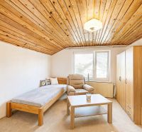 Innenraum eines Einfamilienhauses mit Holzdecke, Sessel und Bett neben dem Fenster.