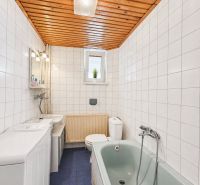Badezimmer mit Fliesen, blauem Boden, Badewanne und Holzdecke in einem Einfamilienhaus.
