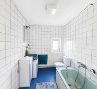 Ein Badezimmer mit Dusche und Badewanne, gefliest mit weißen Fliesen, in einem Einfamilienhaus.