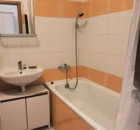 Ein Badezimmer in einer 2-Zimmer-Wohnung mit einer Badewanne und orange-weißen Fliesen.