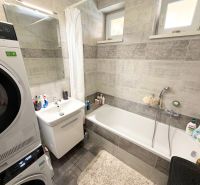 Badezimmer in einem Einfamilienhaus mit Badewanne, Waschbecken und Waschmaschine mit Trockner.