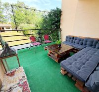 Balkon eines Einfamilienhauses mit Palettensitzmöbeln, grünem Teppich und Blick auf den Garten.
