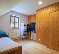 Ein Teil des Schlafzimmers in der Hütte mit einem Bett, einem Fenster und einem Kleiderhaken, Boden mit Holzdekor.