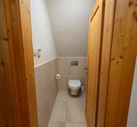Innenraum der Hütte mit WC, helle Fliesen und Holzverkleidung der Wände und Türen.