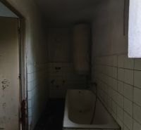 Ein Badezimmer mit Badewanne und Fliesen in einem Einfamilienhaus. An der Wand sind Schäden sichtbar.