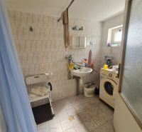 Badezimmer in einem Einfamilienhaus mit Waschmaschine, Duschkabine und kleinem Fenster.