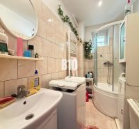 Badezimmer in einem Einfamilienhaus mit Waschmaschine, Badewanne, Waschbecken und Regal mit Produkten.