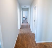Ein Flur in einem Einfamilienhaus mit einem Boden in Holzoptik und weißen Wänden.