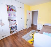 Kinderzimmer in einem Einfamilienhaus mit einem weißen Schrank, einem braunen Bett und einem Boden mit Holzdekor.