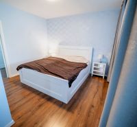 Schlafzimmer in einem Einfamilienhaus mit Bett, Nachttischen und Boden in Holzoptik.