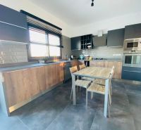 Küche mit Holzdekor, moderne Geräte, geräumiger Tisch und graue Schränke.