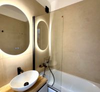 Badezimmer in einer 3-Zimmer-Wohnung mit Badewanne, Waschbecken auf Holzdekor und Spiegel.