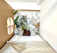 Bett mit gemustertem Überwurf, in einer Einzimmerwohnung mit tropischer Tapete und Kissen.