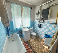 Ein Badezimmer in einem Einfamilienhaus mit älteren hellblauen Fliesen und einer Badewanne.
