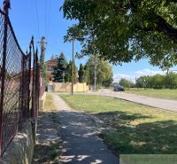 Der Gehweg verläuft entlang des Zauns in den Gärten von Bernolákovo, mit der Straße im Hintergrund.