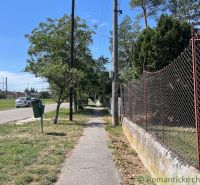 Der Gehweg in Bernolákovo verläuft entlang des Gartenzauns, gesäumt von Bäumen und Gras.
