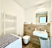 Badezimmer in einer Einzimmerwohnung mit Spiegel, Waschmaschine und Waschbecken mit Holzdekor.