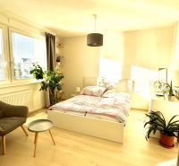 Helles Zimmer in einer Einzimmerwohnung mit Bett und Holzboden.